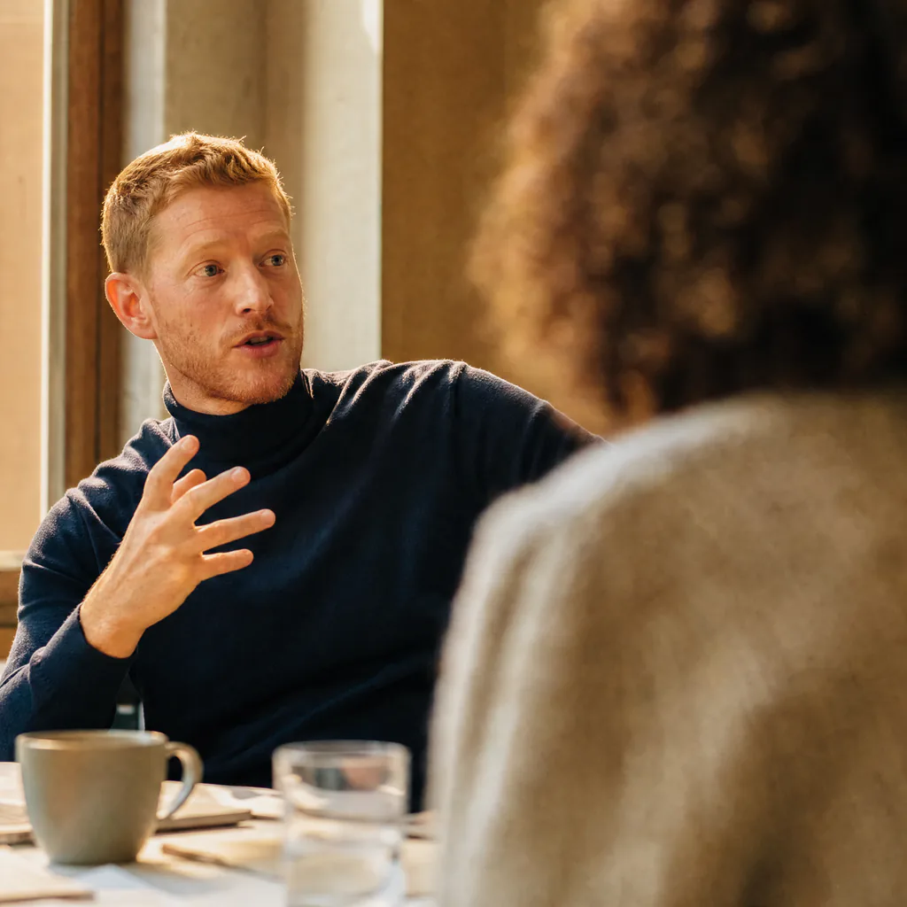 A person gestures while speaking to a colleague across a table