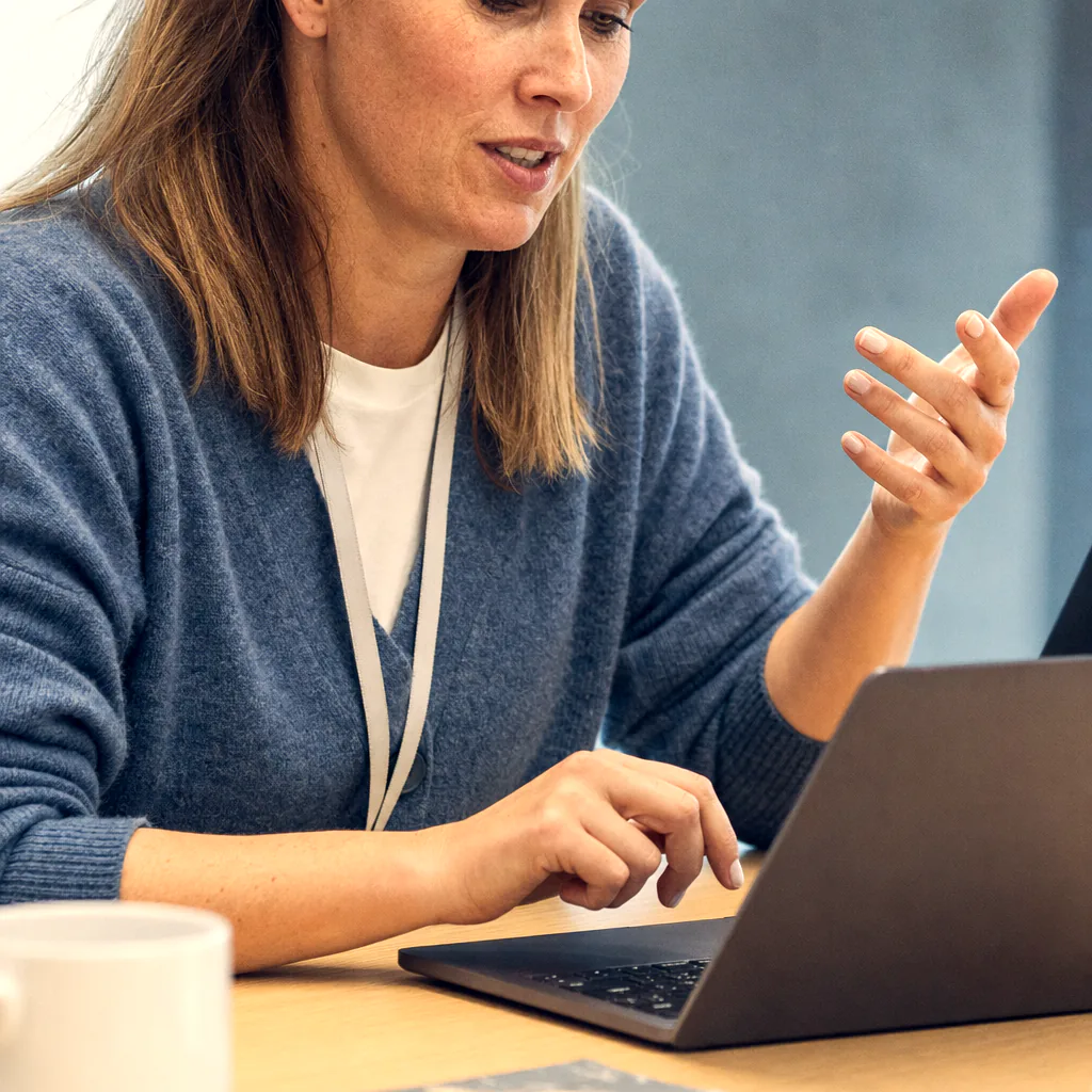 A person gestures while working on a laptop at a table