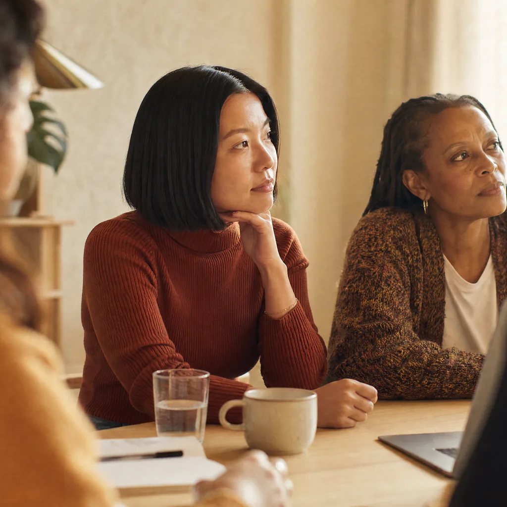 Two people listen to a colleague during a meeting around a table